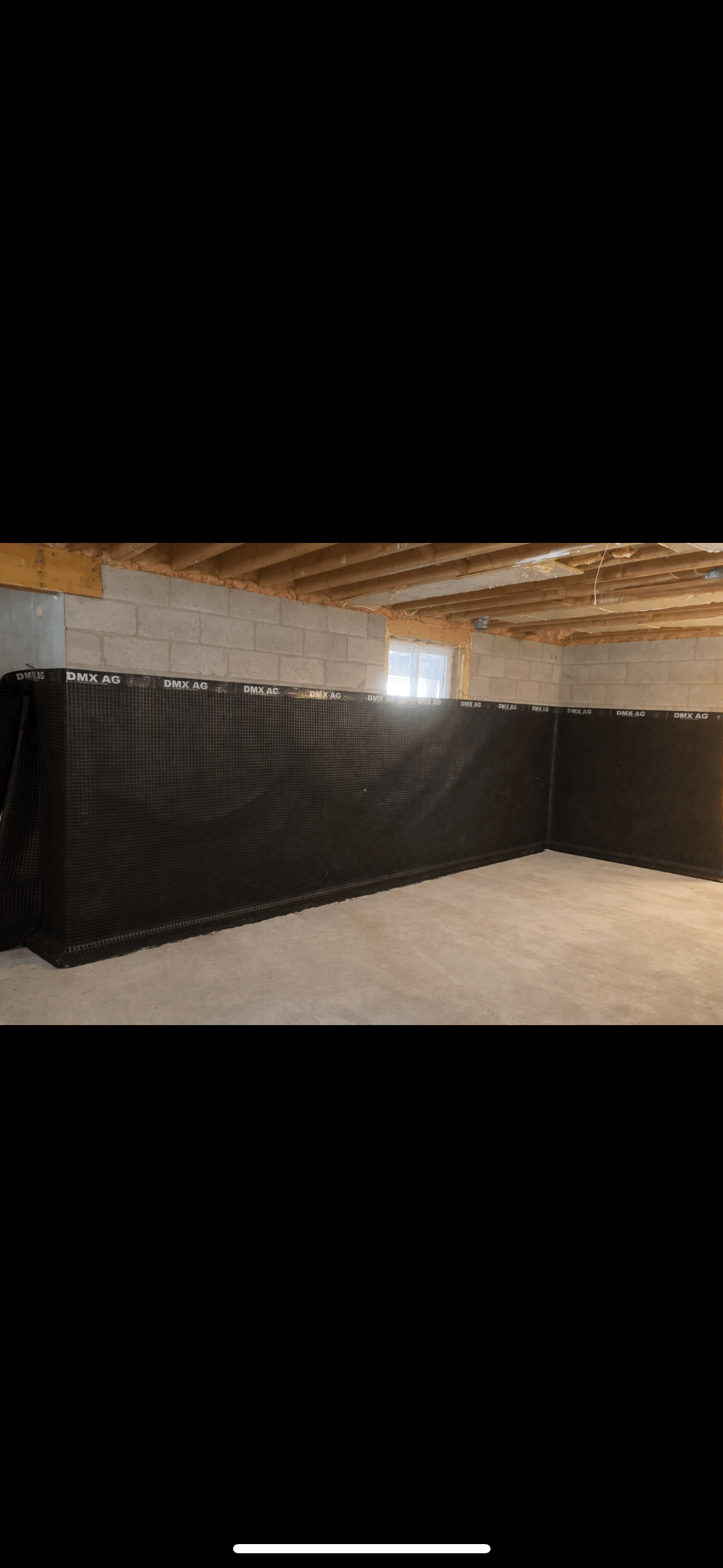 Black dimpled drainage membrane installed along concrete block walls in an unfinished basement.