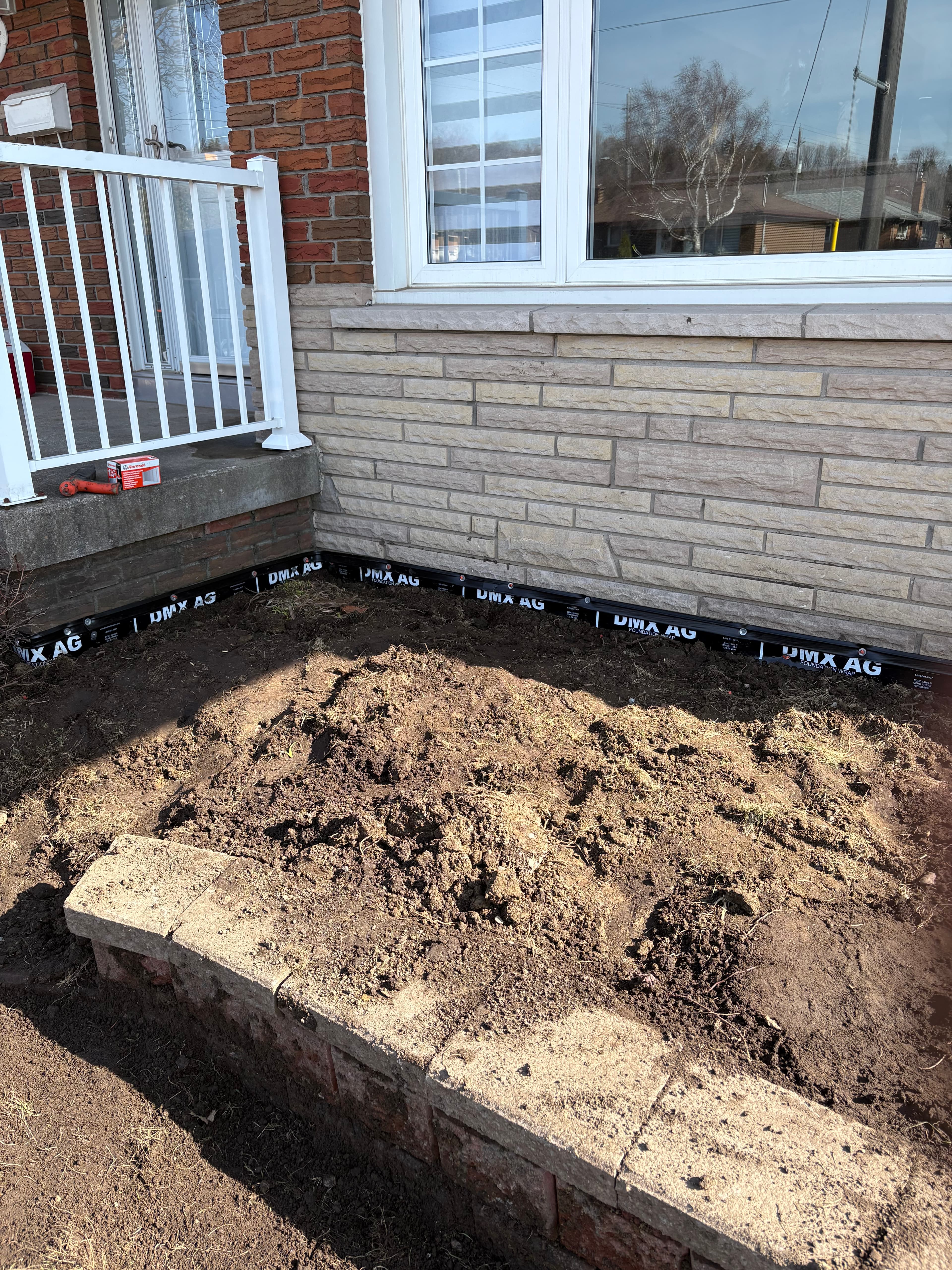 Black foundation wrap installed along a stone wall next to a pile of dirt.